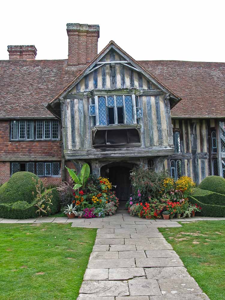 The front aspect of Great dixter House showing the leaning porch with windows above and brightly coloured flowers either side of the entrance door.