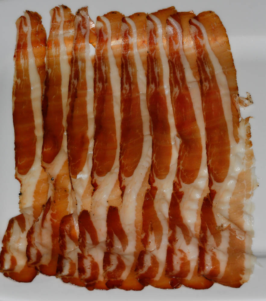 Air dried pancetta cut into very thin slices and laid overlapping across a white serving plate.
