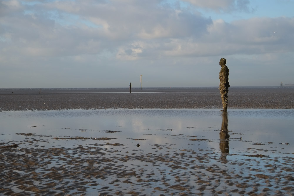 Crosby beach with three cast iron statues and a shipping lane marker visible to the horizon