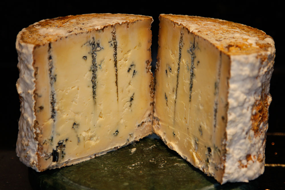 A blue cheese cut in half revealing the blue veined cheese inside.