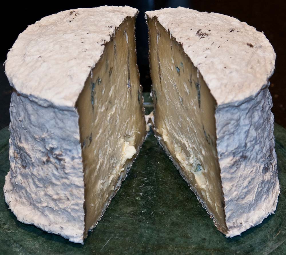 A whole cheese with white mould on the outside and cut open to reveal blue mould on the inside.