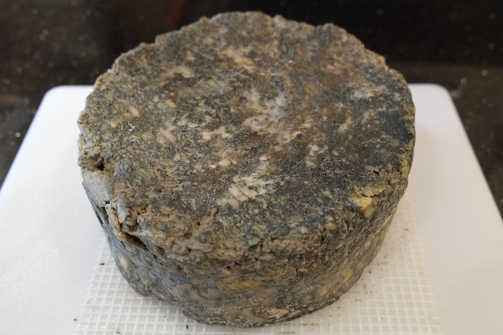 A whole blue cheese showing the thick mouldy rind on the outside.