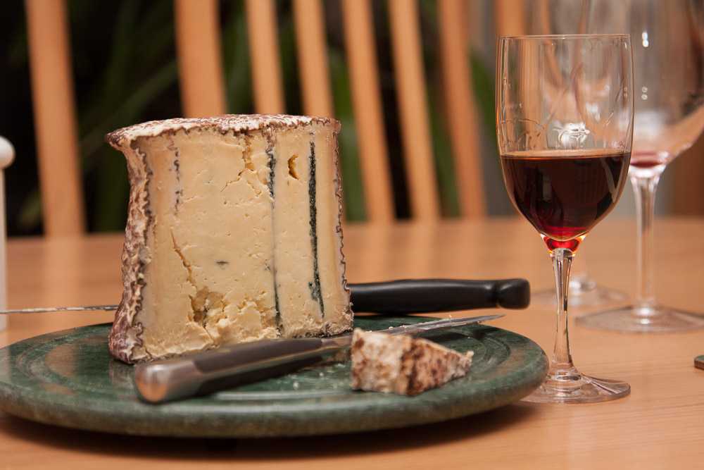 A blue cheese on a green platter with knife next to a glass of Port wine.