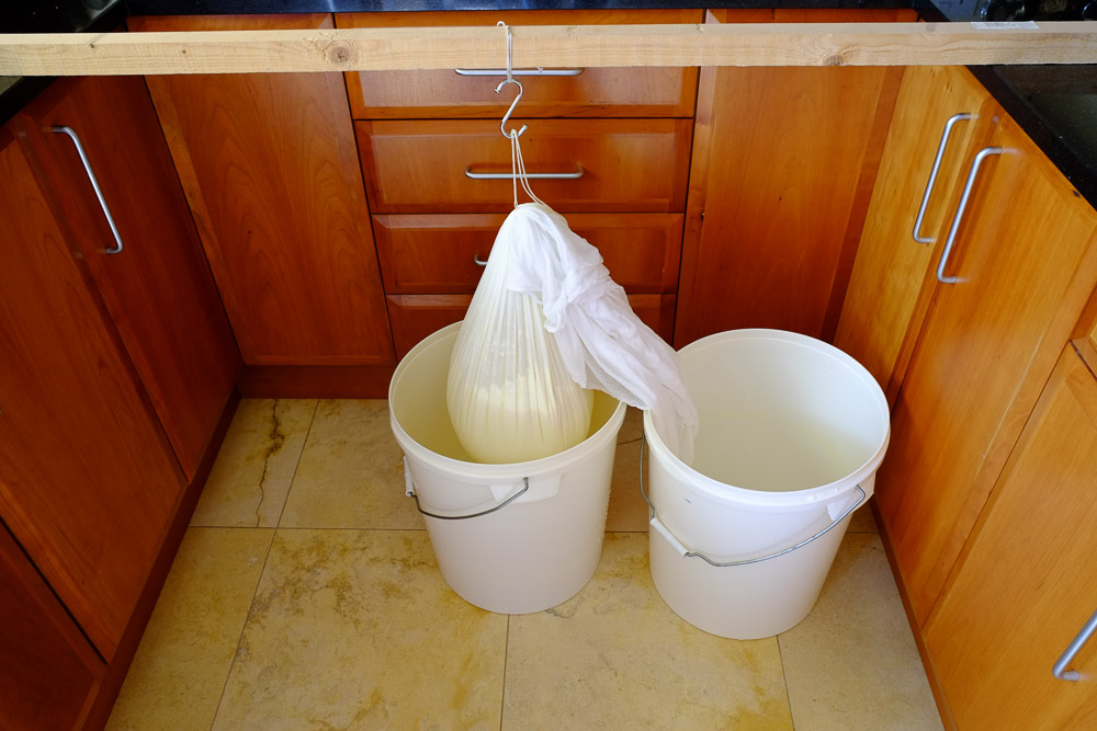Cheese cloth with curds dripping into a plastic bucket