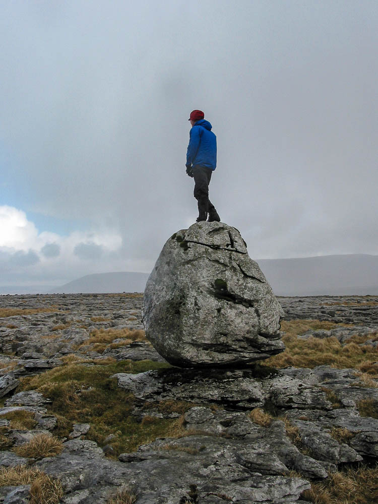 A person standing on top of a large boulder on a limestone moor