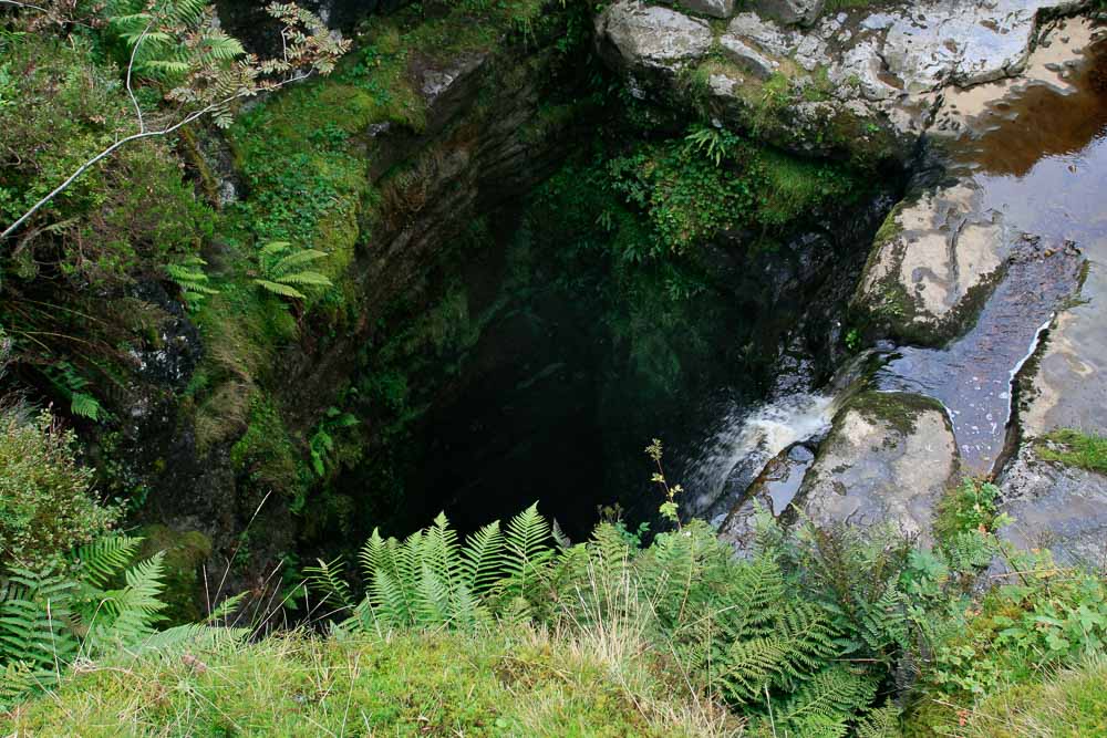 A pothole, Gaping Gill main shaft from above with water flowing into a dark hole