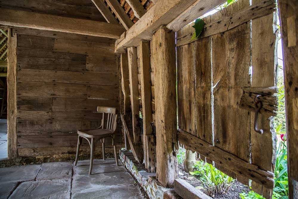 Image of a very old barn with oak panel walls and supports and a wooden chair in the corner.