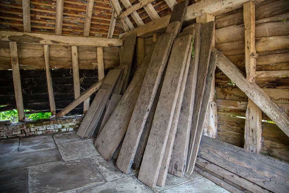 A large number of boards leaning against the old oak walls of a barn. These are the scaffolding boards gardeners use to stand amongst the flower borders.