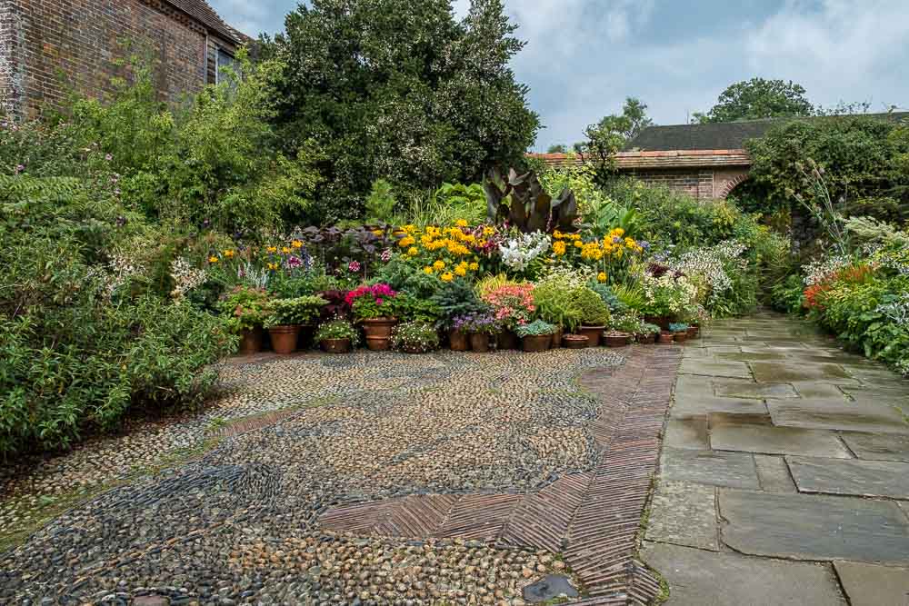 Image of flower pots containing multi coloured flowers on a cobble and slab stone patio.