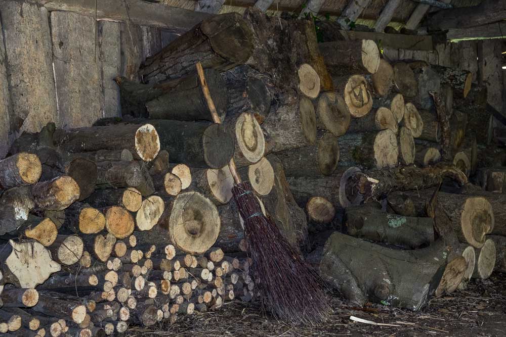 A pile of cut logs in a barn with a traditional bessom or broom leaning against them.