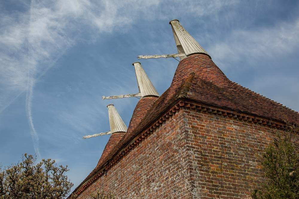 An oast house with three white cowls atop a terracotta tiled roof against a blue sky