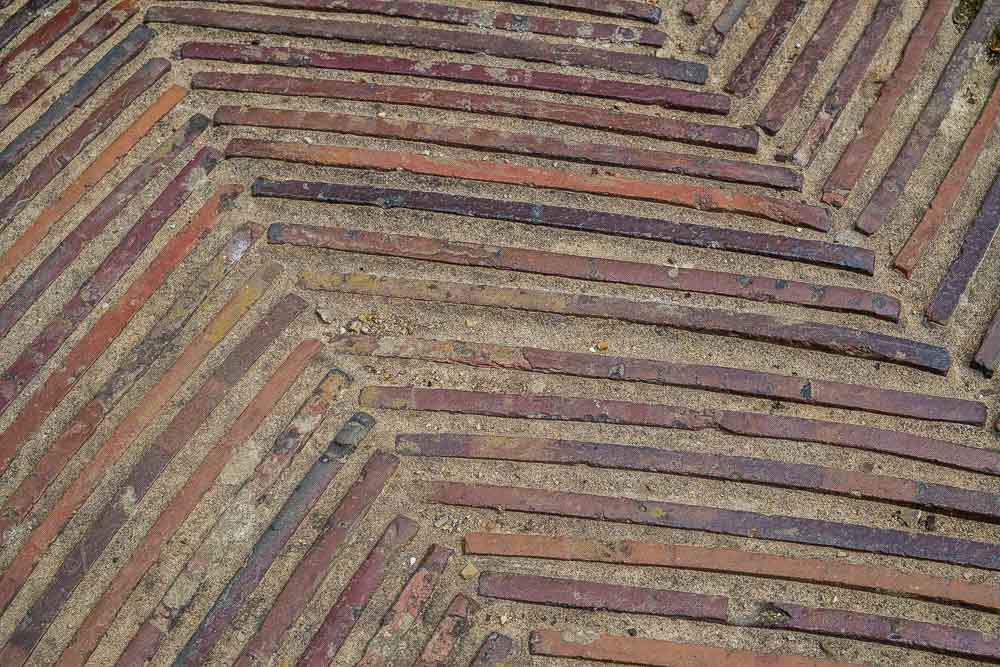 Close up image of a patio made with inlaid terracotta roof tiles laid on their edge in mortar.