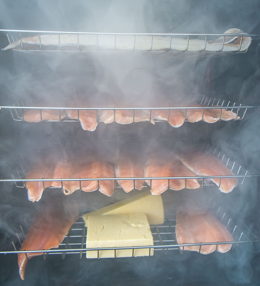 A view inside a smoking cabinet showing fish and cheese in a smoky atmosphere.