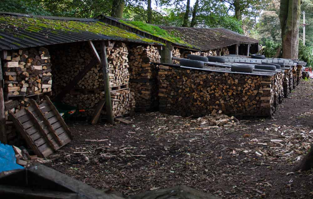 Logs stored in neat piles in sheds and under covers weighted down with old tyres