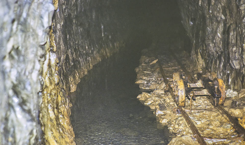 A mine tunnel with an old rail and bogey visible alongside a stream