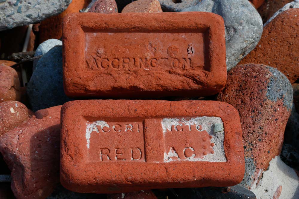 Two red bricks that have been eroded by the sea. One has Accrington and the other has Accrington REDAC embossed into the surface.