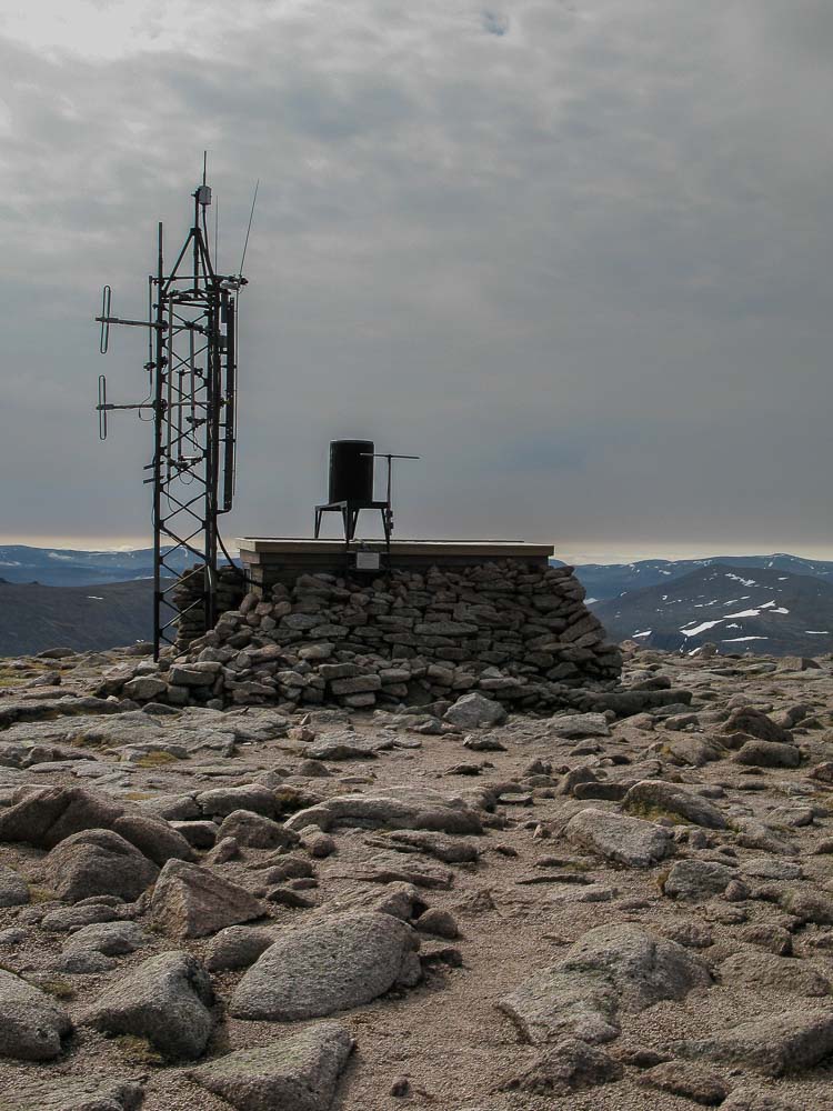 A flat rocky mountain top with aerials and a barrel type contraption atop a stone and concrete platform