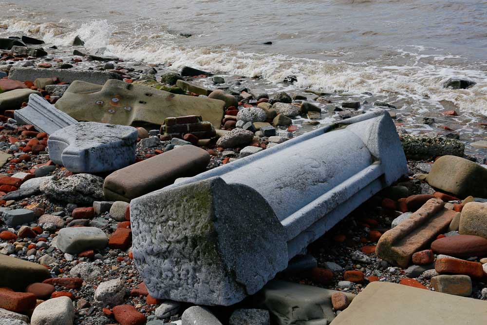 A large piece of carved grey granite lying on a beach with waves lapping at one end