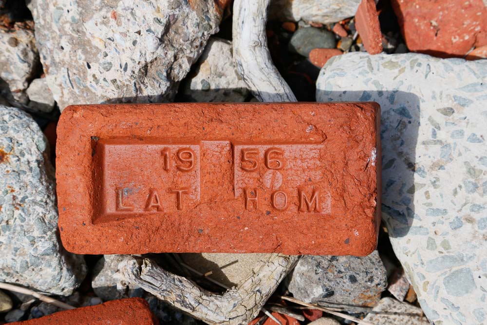 A red brick lying on a beach with 1956 Latholm embossed in the top