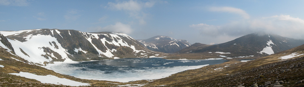 A part frozen and snow covered lake seen from above with snow speckled mountains around it