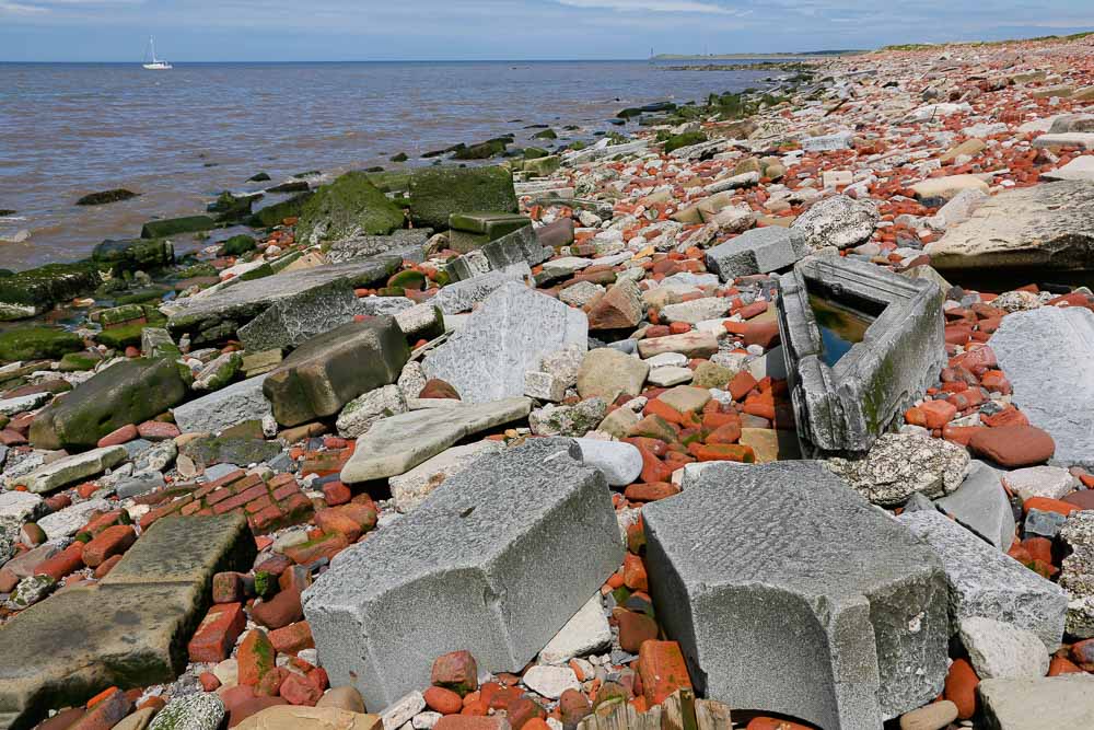 A beach scene with the beach entirely covered in building rubble including some large ornately carved stone architectural pieces