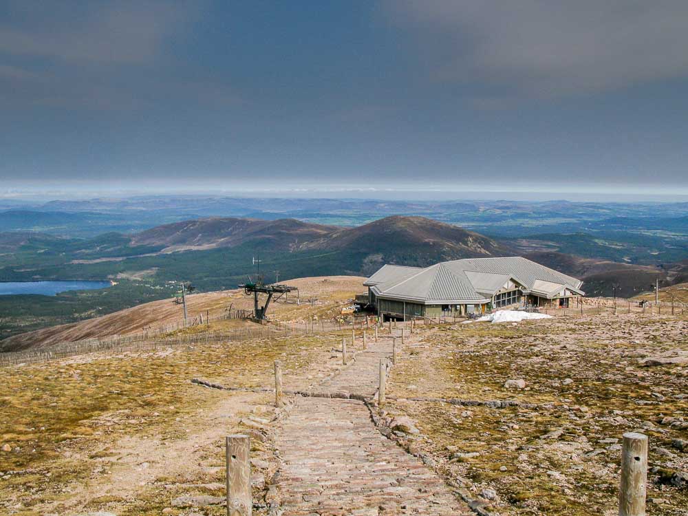 A view from the summit of Cairngorm looking down on a stone path leading down to the Ptarmigan Restaurant with Loch Morlich in the distance
