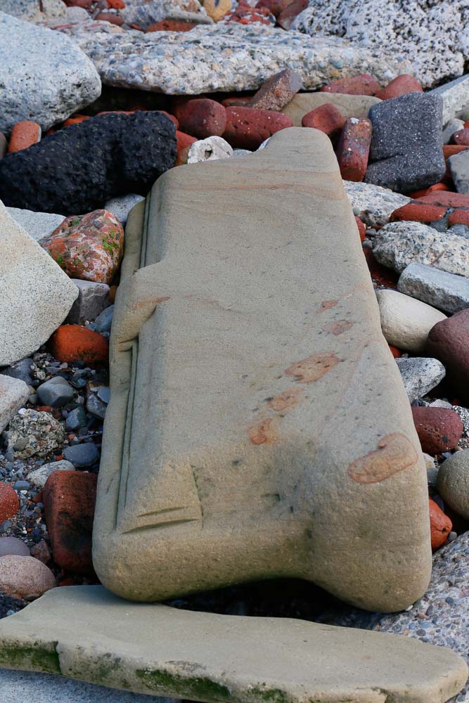 A large piece of carved sandstone, water warn from years of lying on the beach