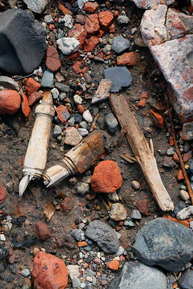 Pieces of a broken wooden table leg lying amongst stone and brick debris on a beach